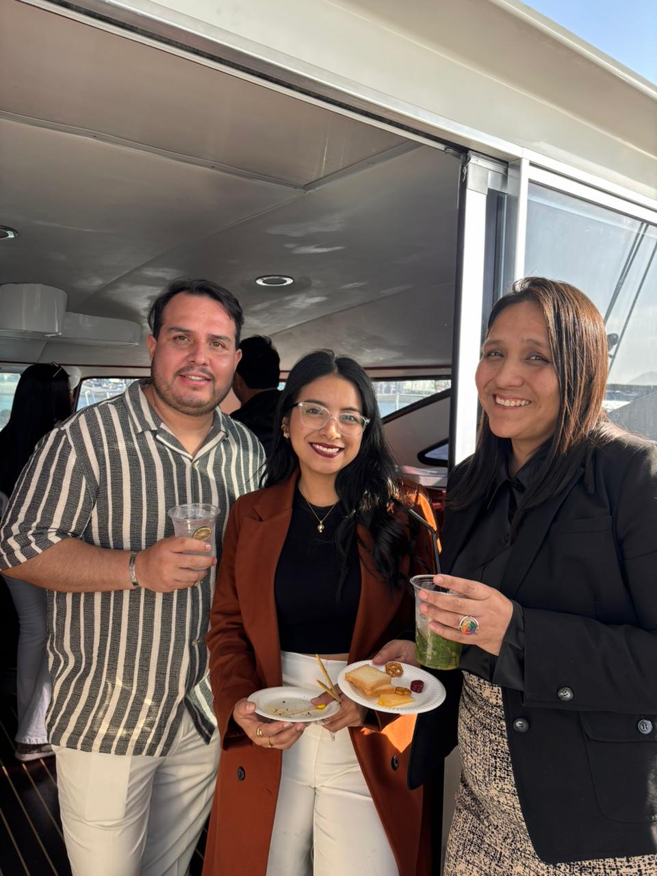 Tres asistentes brindando con copas y platos en la mano